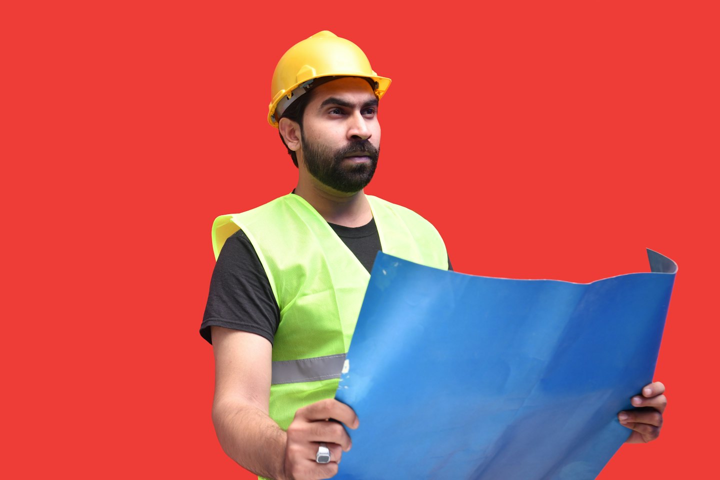 Man in hard hat reviews blueprints at a desk.